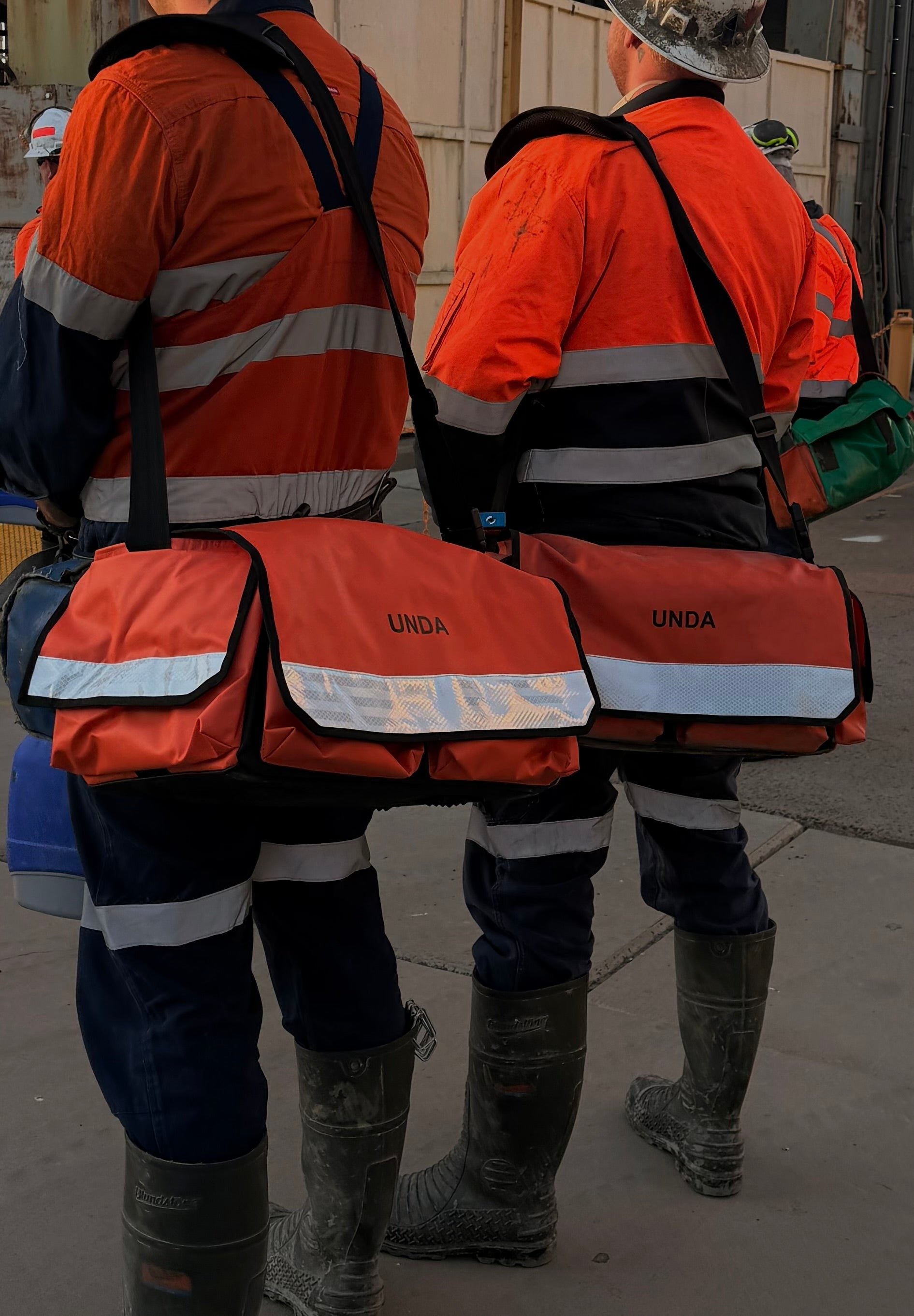 Two workers in hi-vis carrying UNDA Tool-Mate bags on a mine site
